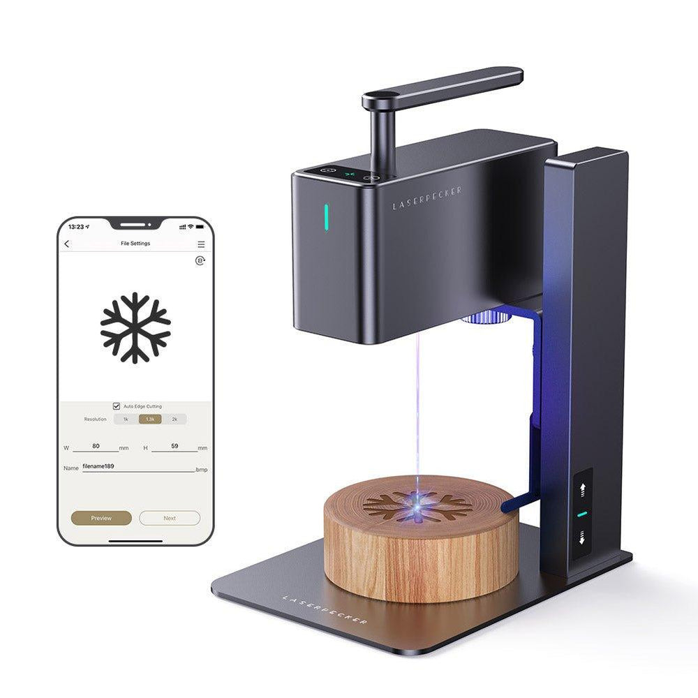レーザー彫刻機とスマートフォンの操作画面。木製円盤に雪の結晶模様を彫刻している。