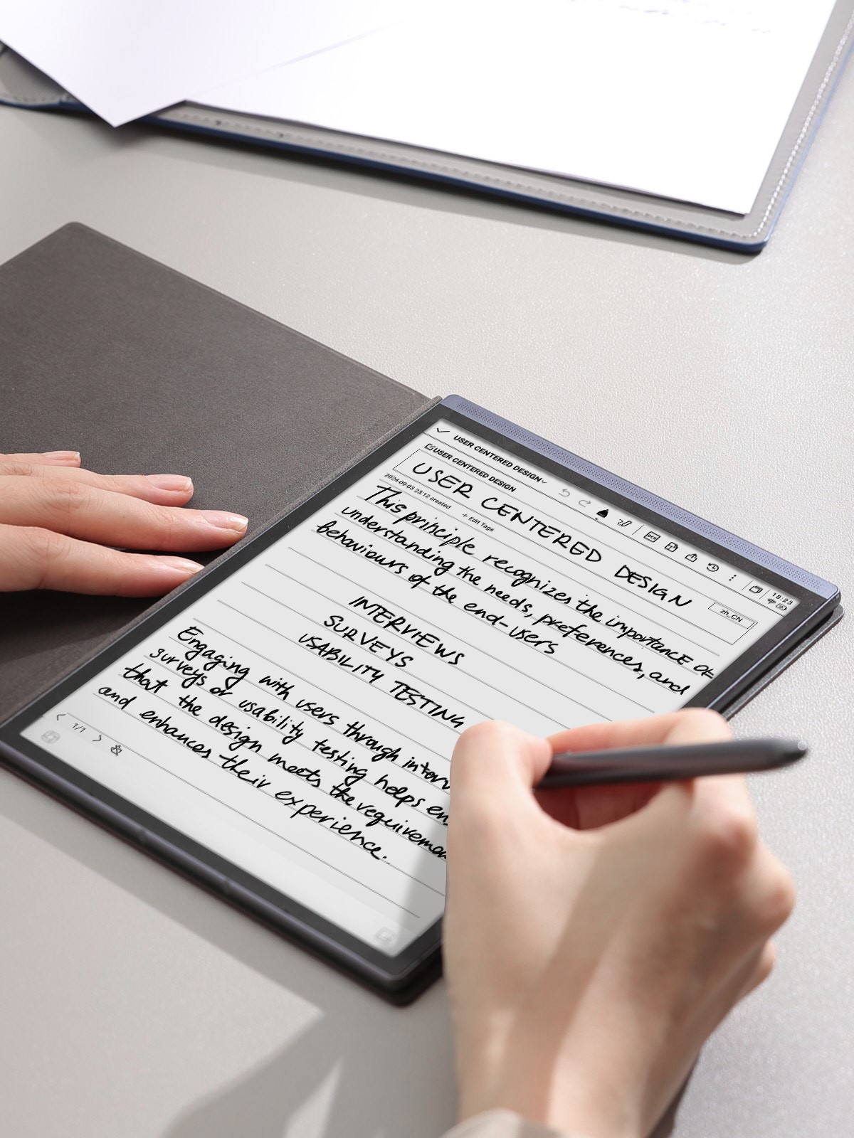 電子書籍リーダーにペンで手書き入力している様子。デスクには複数のデバイスが置かれている。