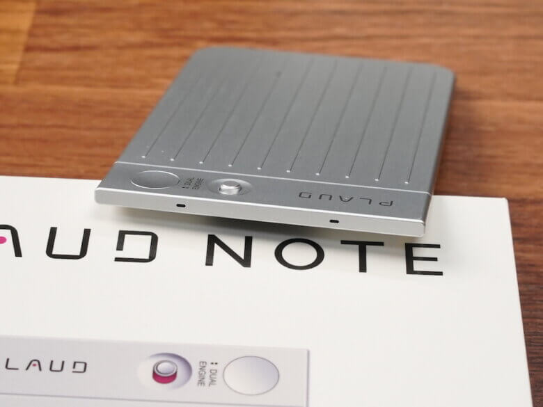 PLAUDOというポータブルオーディオデバイスが木製テーブルの上に置かれている。